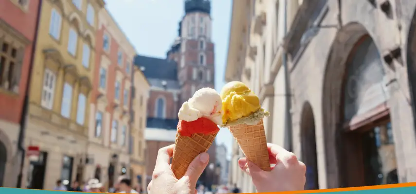 Two gelato cones held up on a summer day in Kraków's Old Town, with the towers of St. Mary's Basilica in the background.