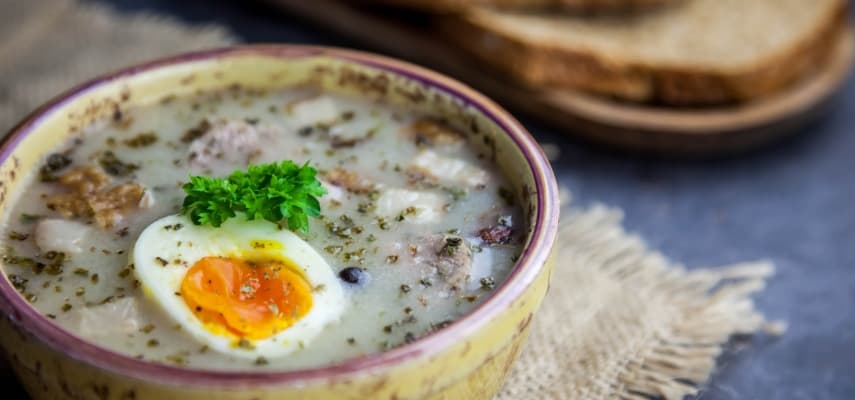 Żurek, the tangy Polish sour rye soup, served with slices of white sausage and hard-boiled egg in a ceramic bowl.