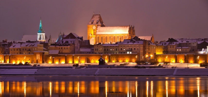 The Gothic Old Town Hall and surrounding brick architecture of medieval Toruń seen from the Vistula riverbank.