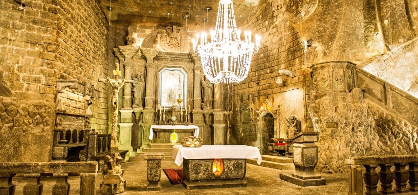 Underground chamber of the Wieliczka Salt Mine with salt-carved sculptures lit by chandeliers.